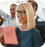 Jubelnde Personen vor Flipchart, blonde, lachende Frau mit Brille im Vordergrund